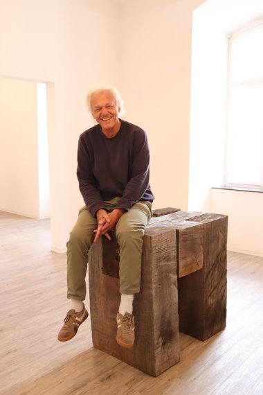 Artist sits on wooden work of art
